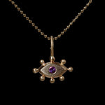 Gold pendant with with an eye design and purple gemstone on a black background