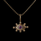 Gold pendant with with an eye design and purple gemstone on a black background