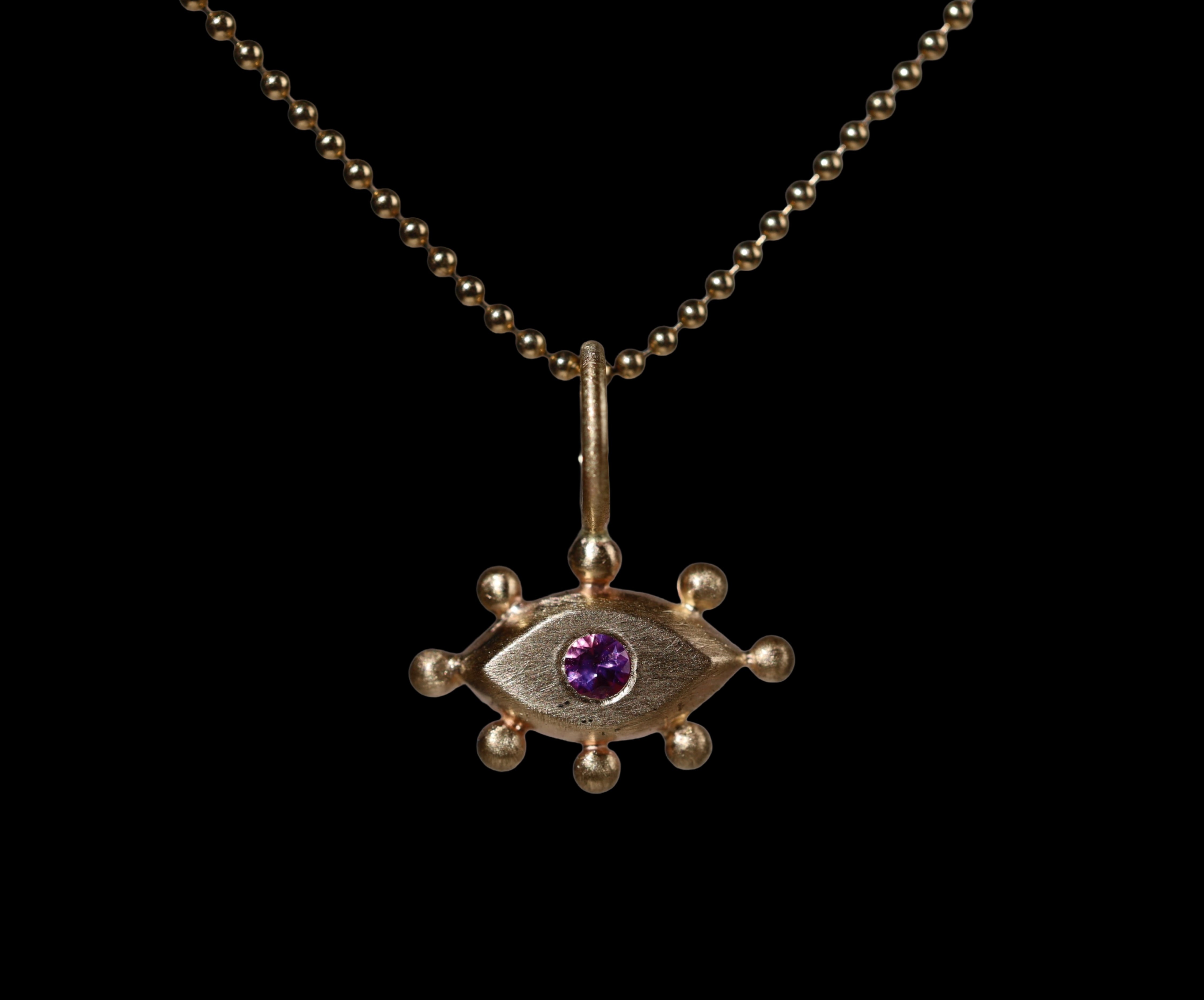 Gold pendant with with an eye design and purple gemstone on a black background