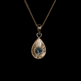 Gold pendant with an ocean blue Montana sapphire on a black background