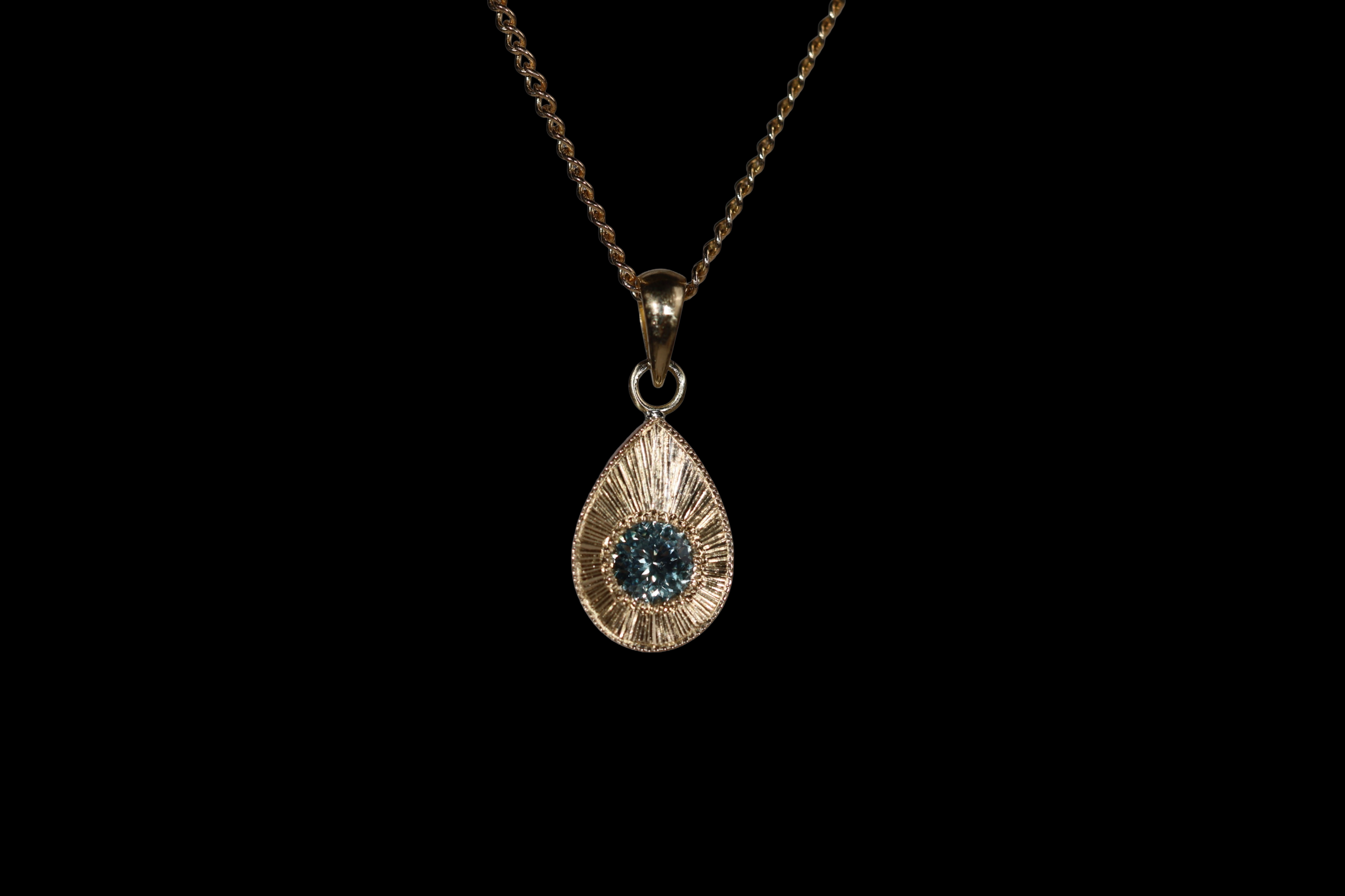 Gold pendant with an ocean blue Montana sapphire on a black background