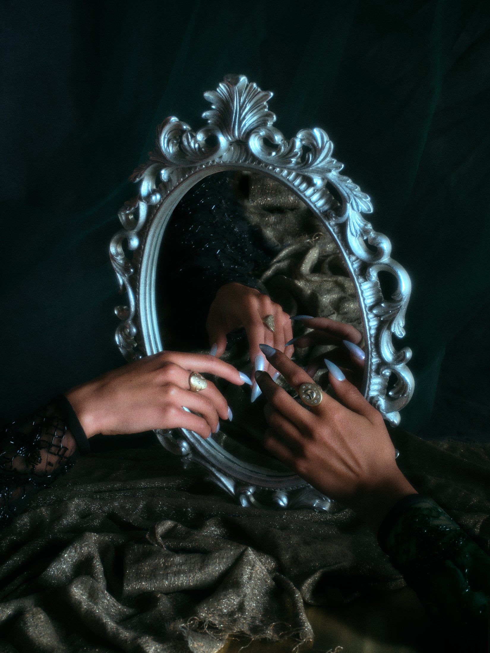 Models hands with wearing 18k hand-engraved diamond moon ring along with other jewelry in front of a baroque mirror and dark backdrop.