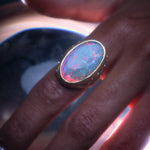 Closeup of moonage daydream ring on model's hand emphasizing the play of colors within the opal.