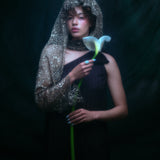 Model wearing the moonage daydream ring on her pointer finger while holding a large white lily against a dark background.