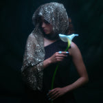 Model wearing the moonage daydream ring on her pointer finger while holding a large white lily against a dark background.