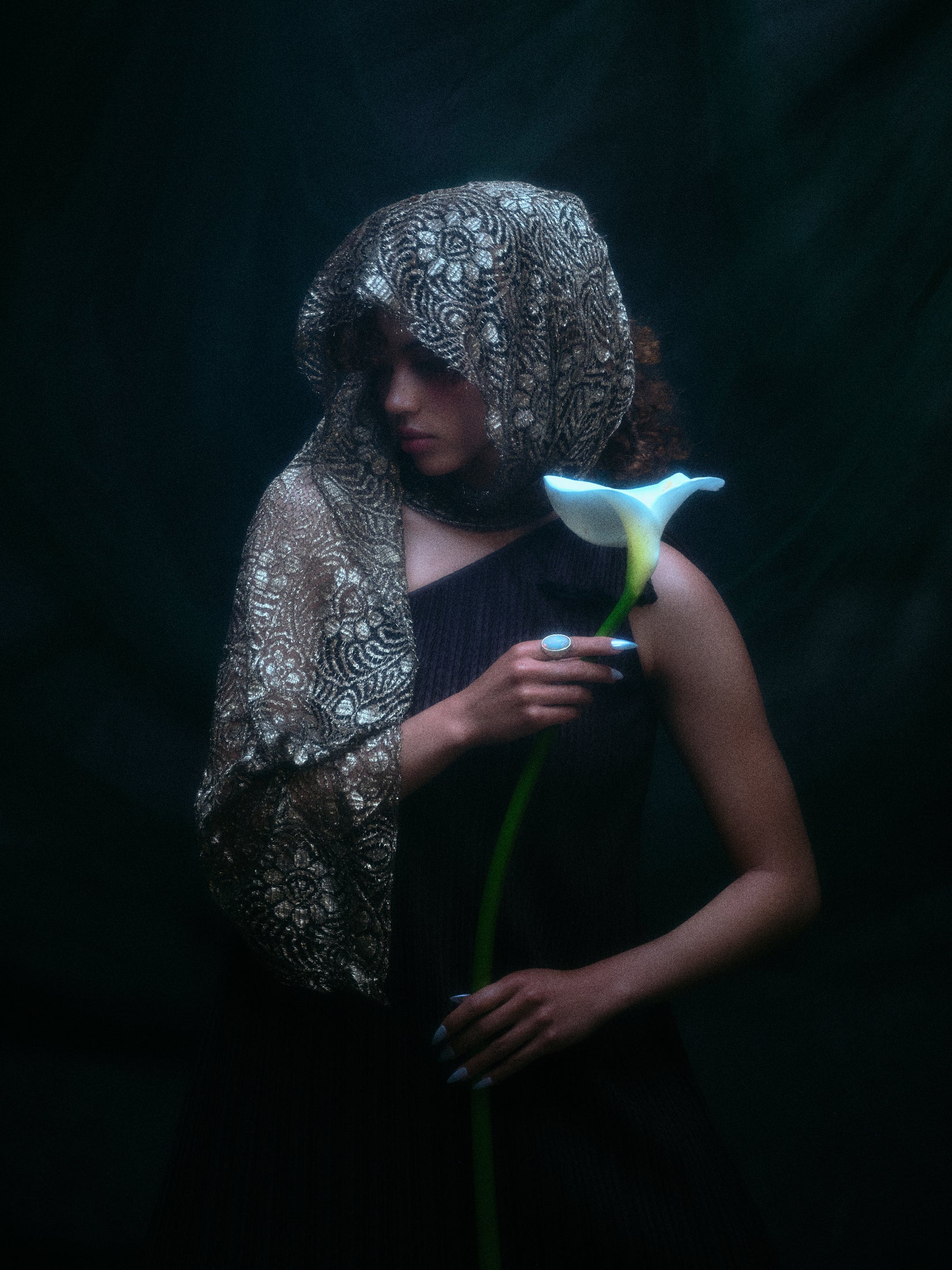 Model wearing the moonage daydream ring on her pointer finger while holding a large white lily against a dark background.