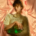 Model wearing 14k emerald and ruby necklace along with emerald ruby earrings and other jewelry against a pink silk background.