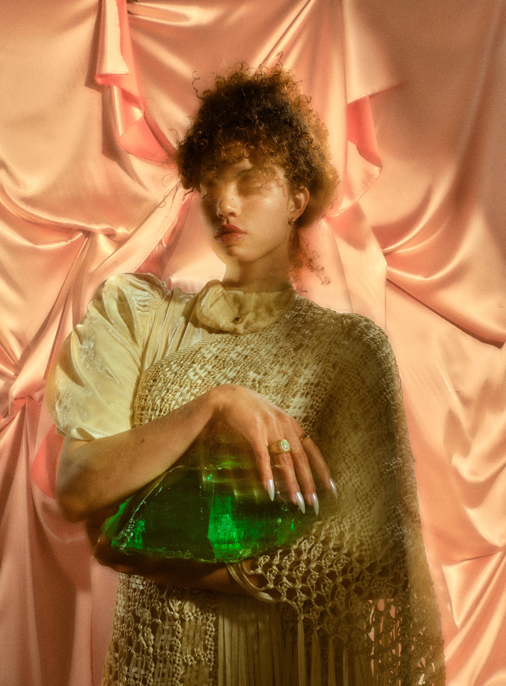 Model wearing 14k emerald and ruby necklace along with emerald ruby earrings and other jewelry against a pink silk background.