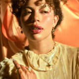 Model wearing 14k emerald and ruby necklace along with emerald ruby earrings and other jewelry against a pink silk background.