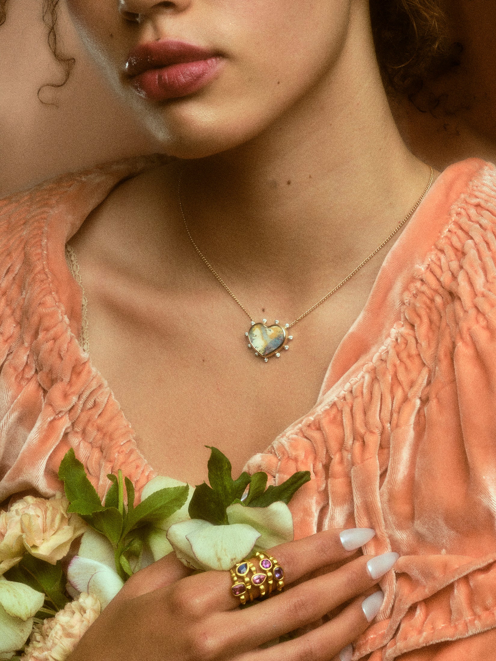 Model wearing stack of five hydria inspired rings on pointer finger and a heart pendant necklace.