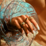 Model's hand with a stack of hydria inspired rings on her pointer finger along with rings on other fingers.
