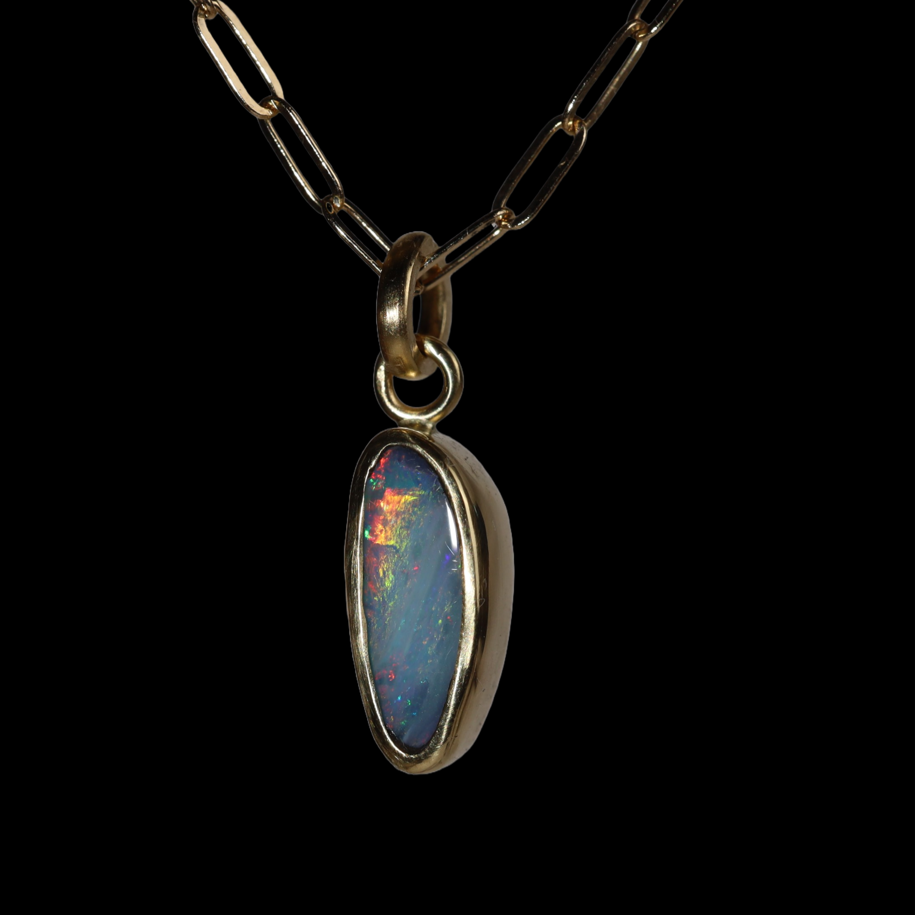 Three quarter view of tall oval opal  pendant with green, red, and blue sparkle.