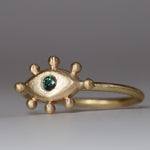 Gold ring with eye design and bottle green  on a gray background
