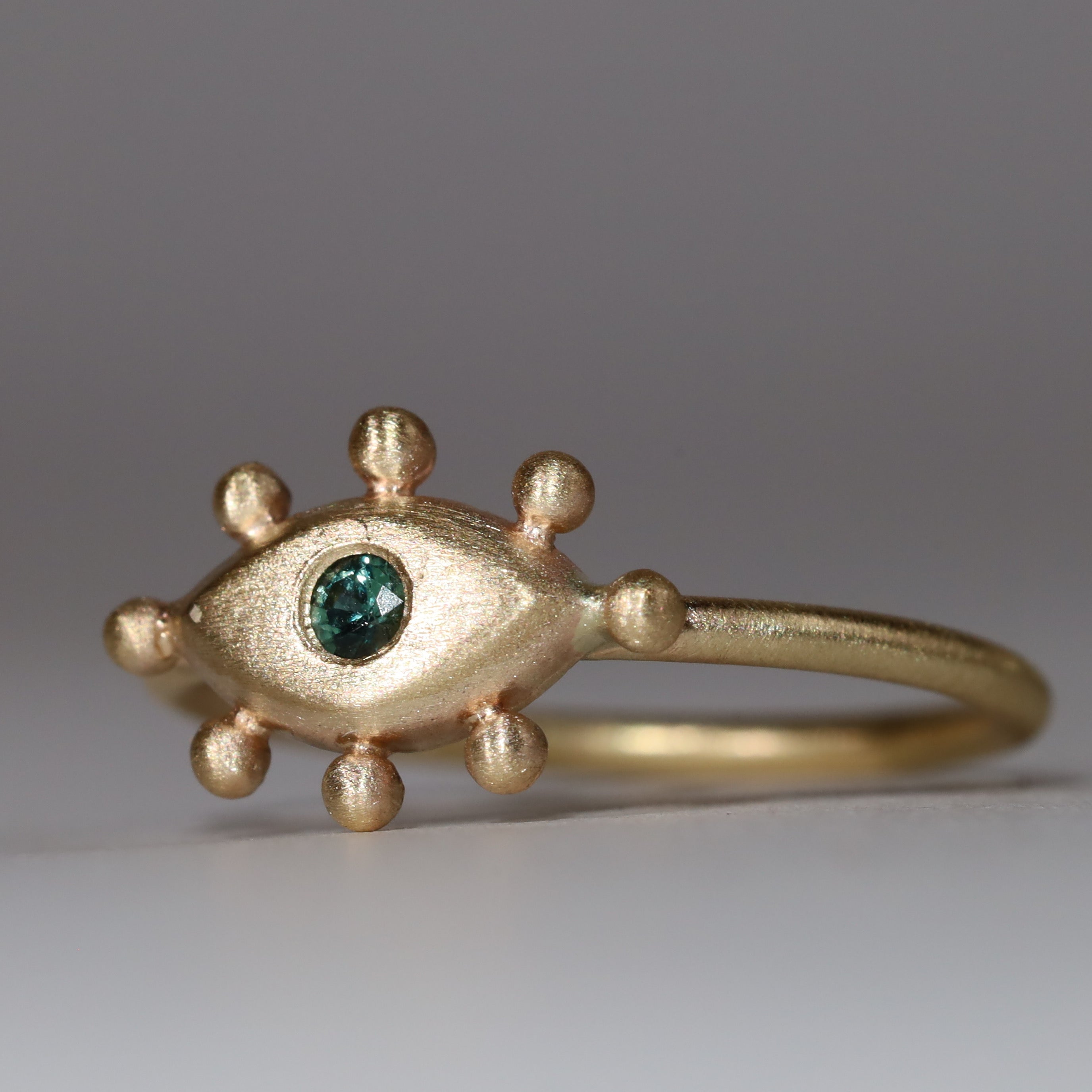 Gold ring with eye design and bottle green  on a gray background