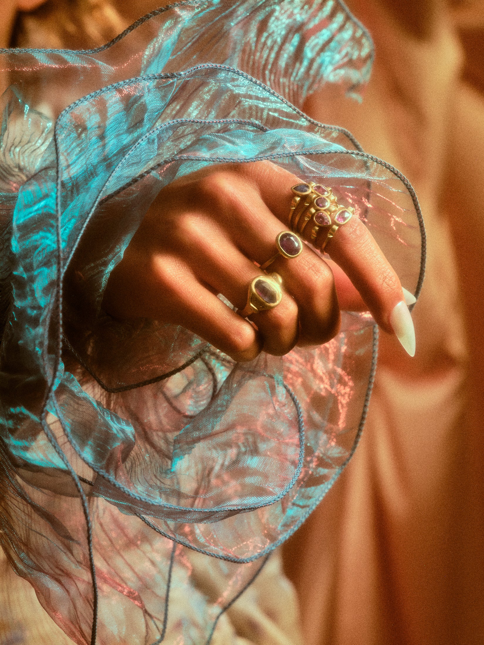 Alternate view of model's hand with grape colored sapphire ring on her middle  finger along with rings on other fingers.