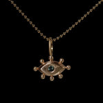 Gold pendant with with an eye design and green gemstone on a black background