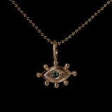 Gold pendant with with an eye design and green gemstone on a black background
