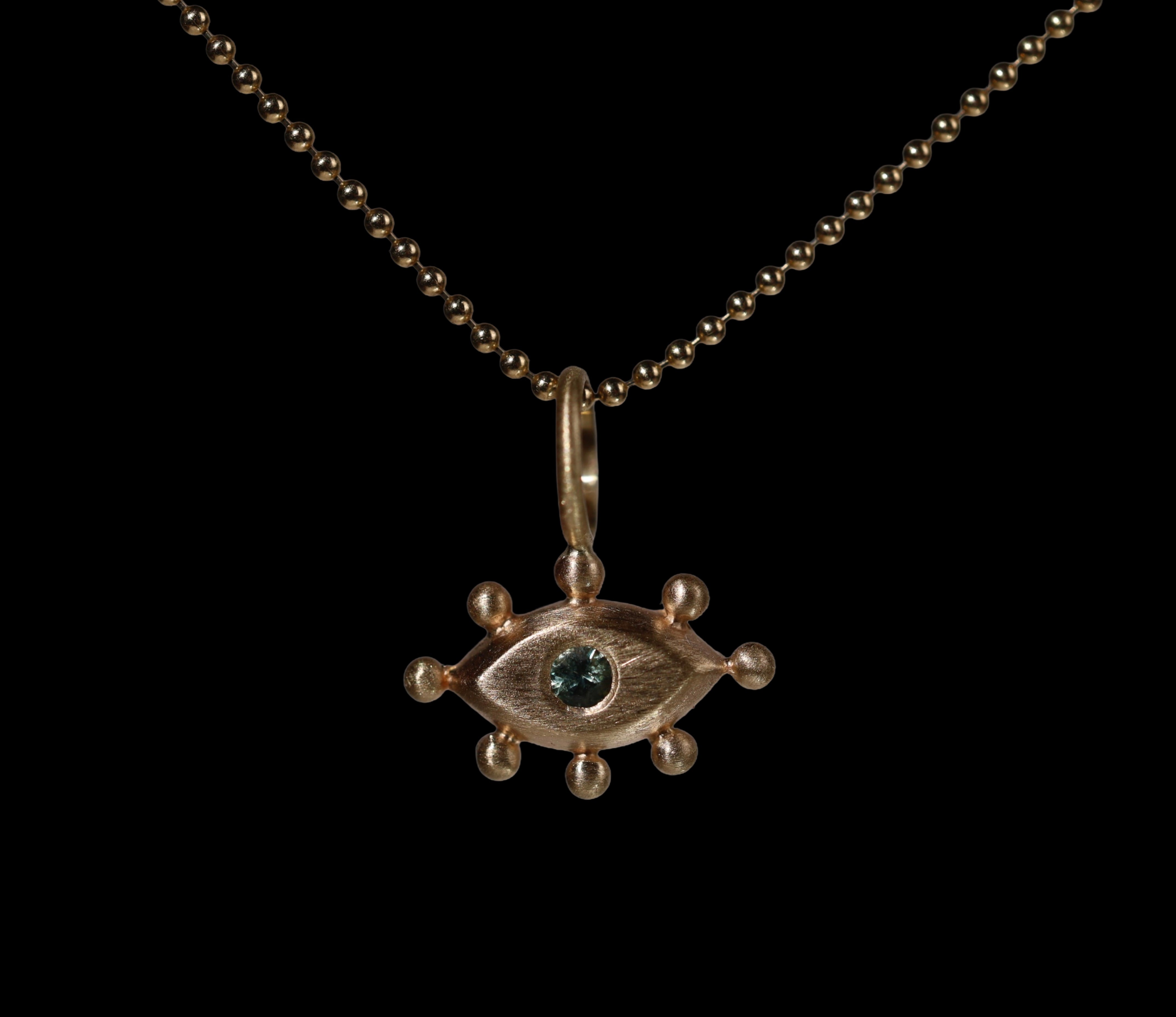 Gold pendant with with an eye design and green gemstone on a black background