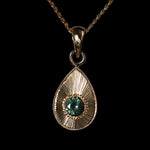 Gold teardrop pendant with a large blue green sapphire on a black background.