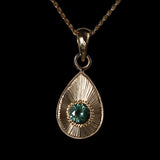 Gold teardrop pendant with a large blue green sapphire on a black background.