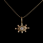 Gold pendant with with an eye design and diamond on a black background