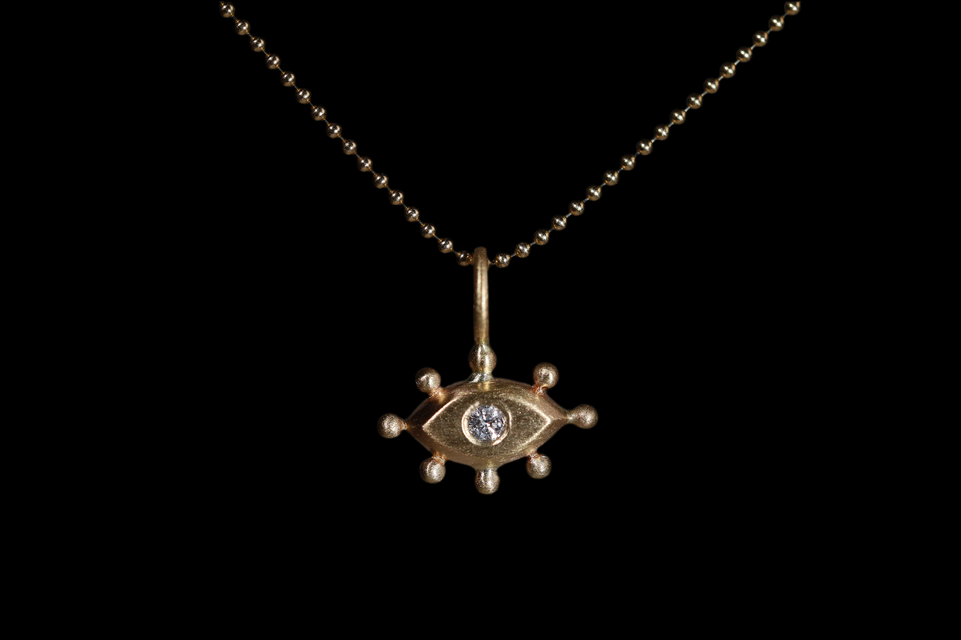 Gold pendant with with an eye design and diamond on a black background