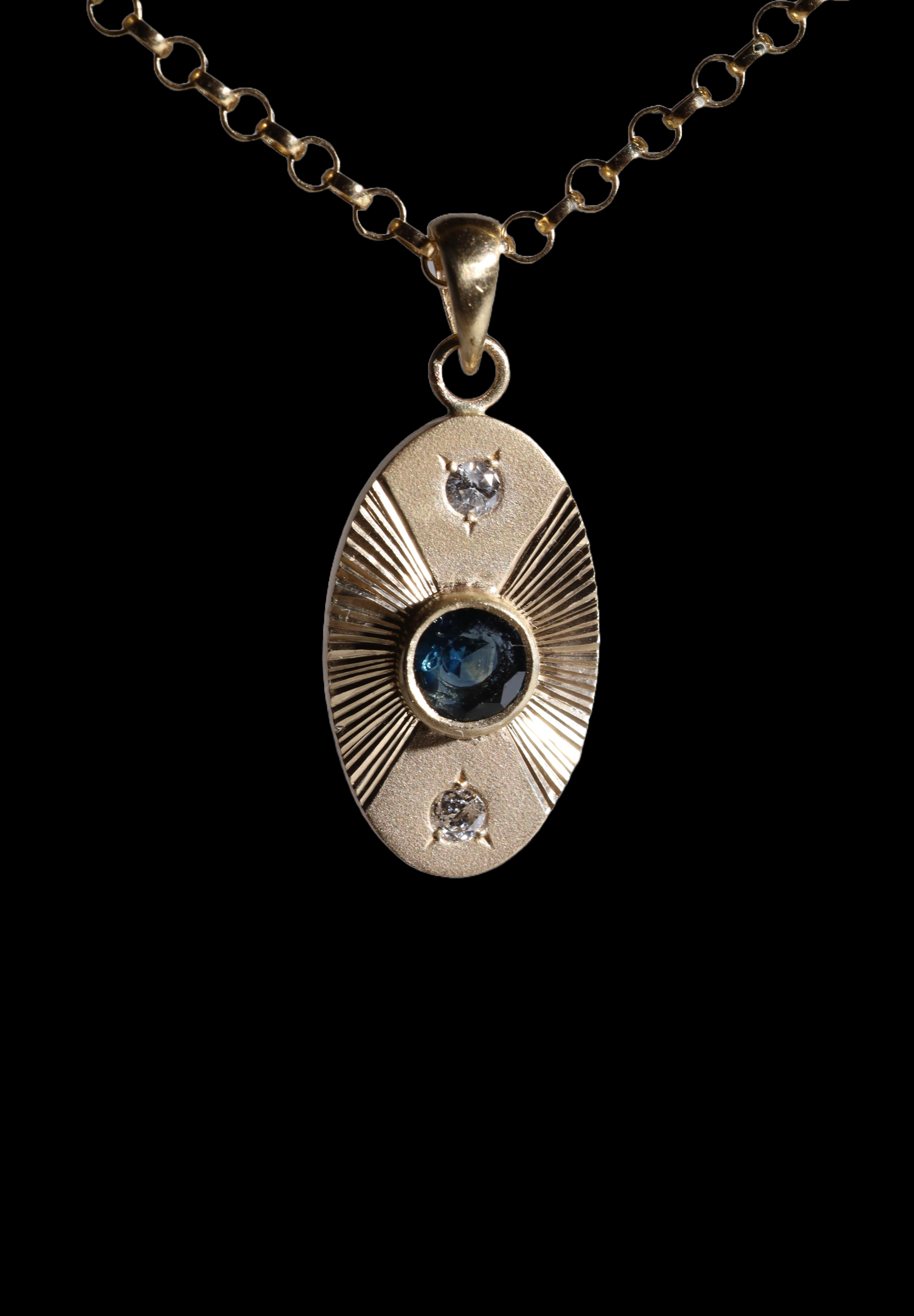 Front view of 14k yellow gold portal charm.  Tall oval shaped with central set blue sapphire, white diamonds set top and bottom and engraved lines radiating to the left and right.  Attached to separately available yellow gold chain.