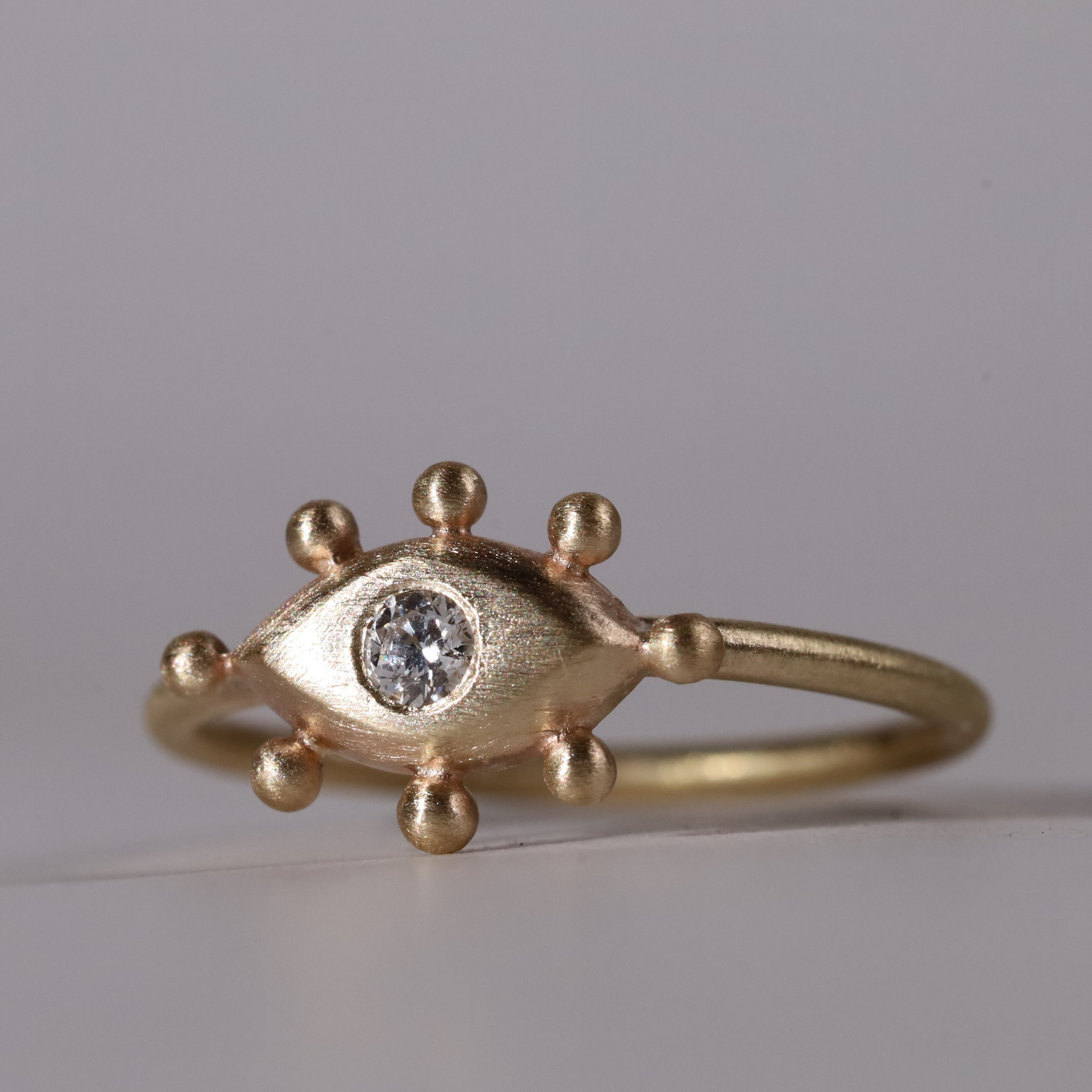 Gold ring with eye design and diamond on a gray background