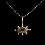 Gold pendant with with an eye design and blue gemstone on a black background