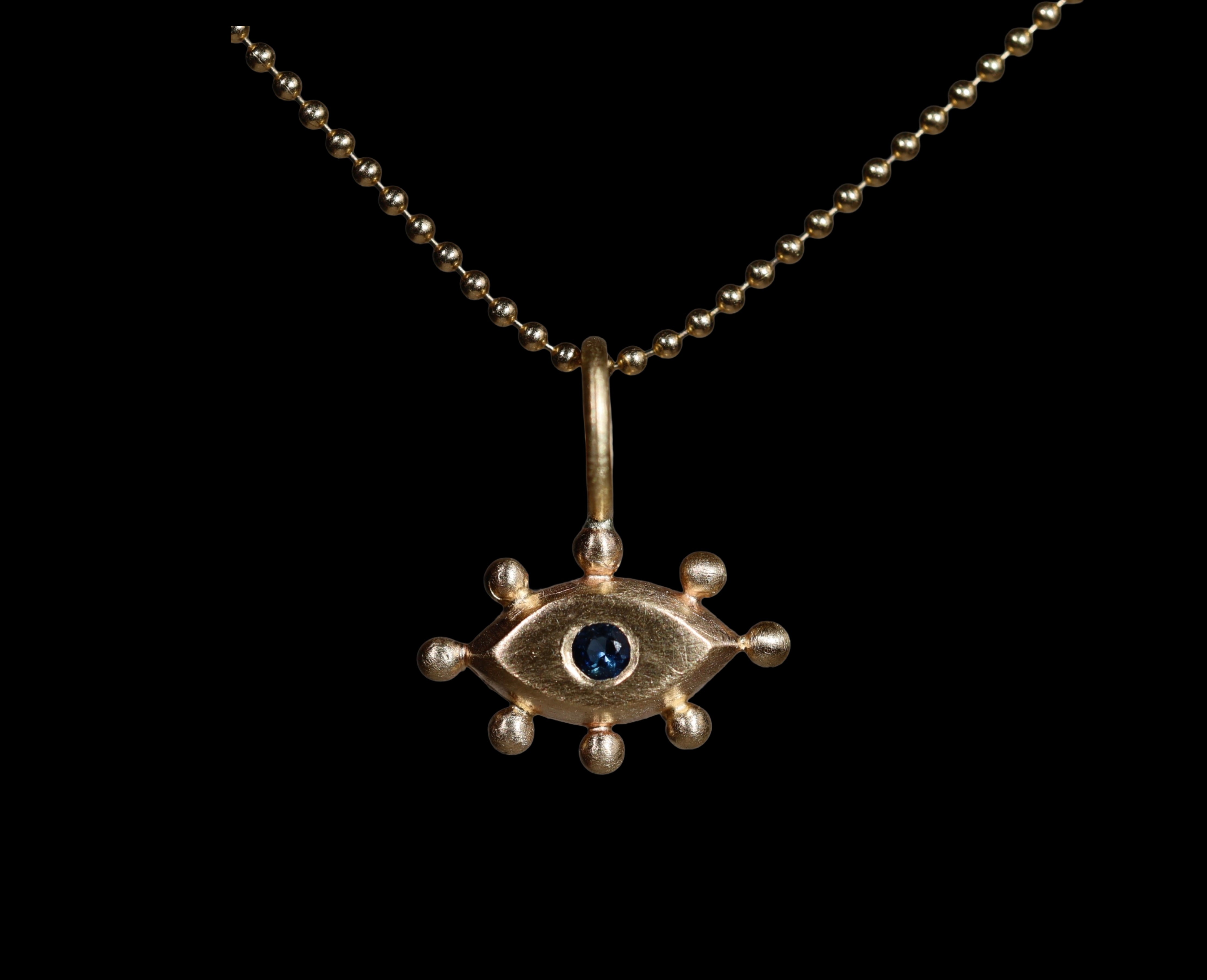 Gold pendant with with an eye design and blue gemstone on a black background