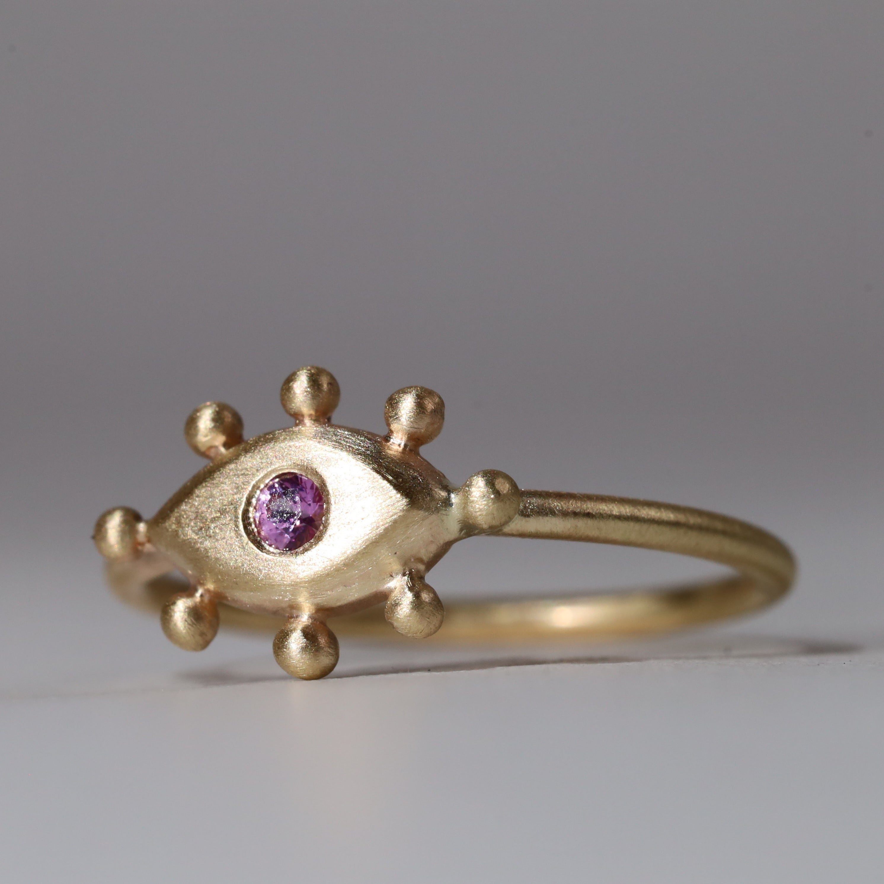 Gold ring with eye design and ballet pink gemstone on a gray background