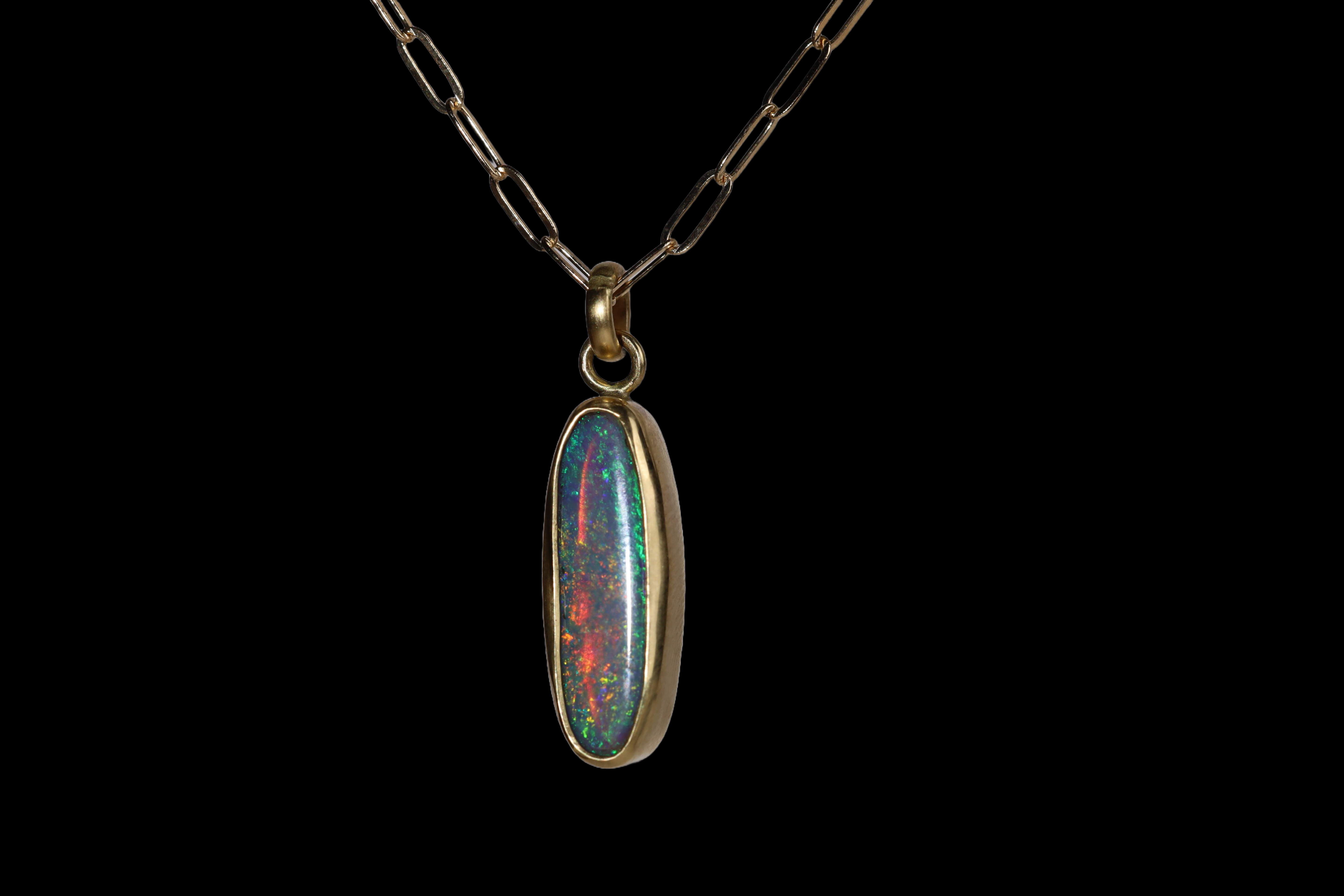 Three quarter view of tall oval pendant with green, blue, and red sparkle.