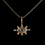 Gold pendant with with an eye design and purple gemstone on a black background