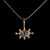 Gold pendant with with an eye design and purple gemstone on a black background