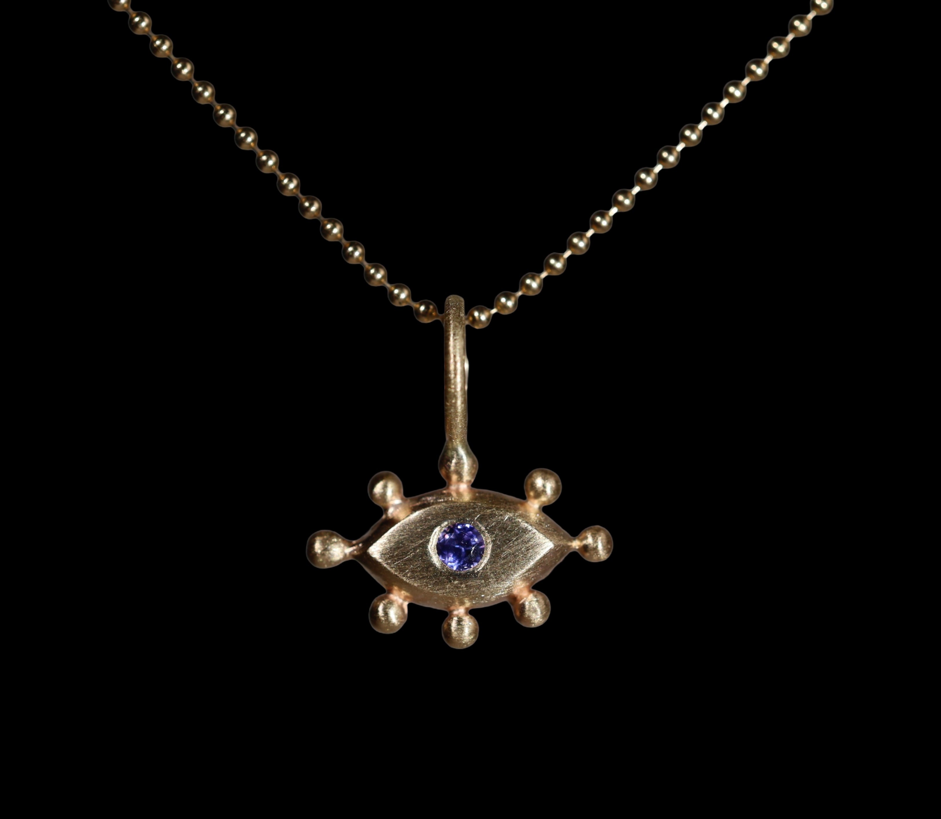 Gold pendant with with an eye design and purple gemstone on a black background