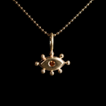 Gold pendant with with an eye design and orange gemstone on a black background