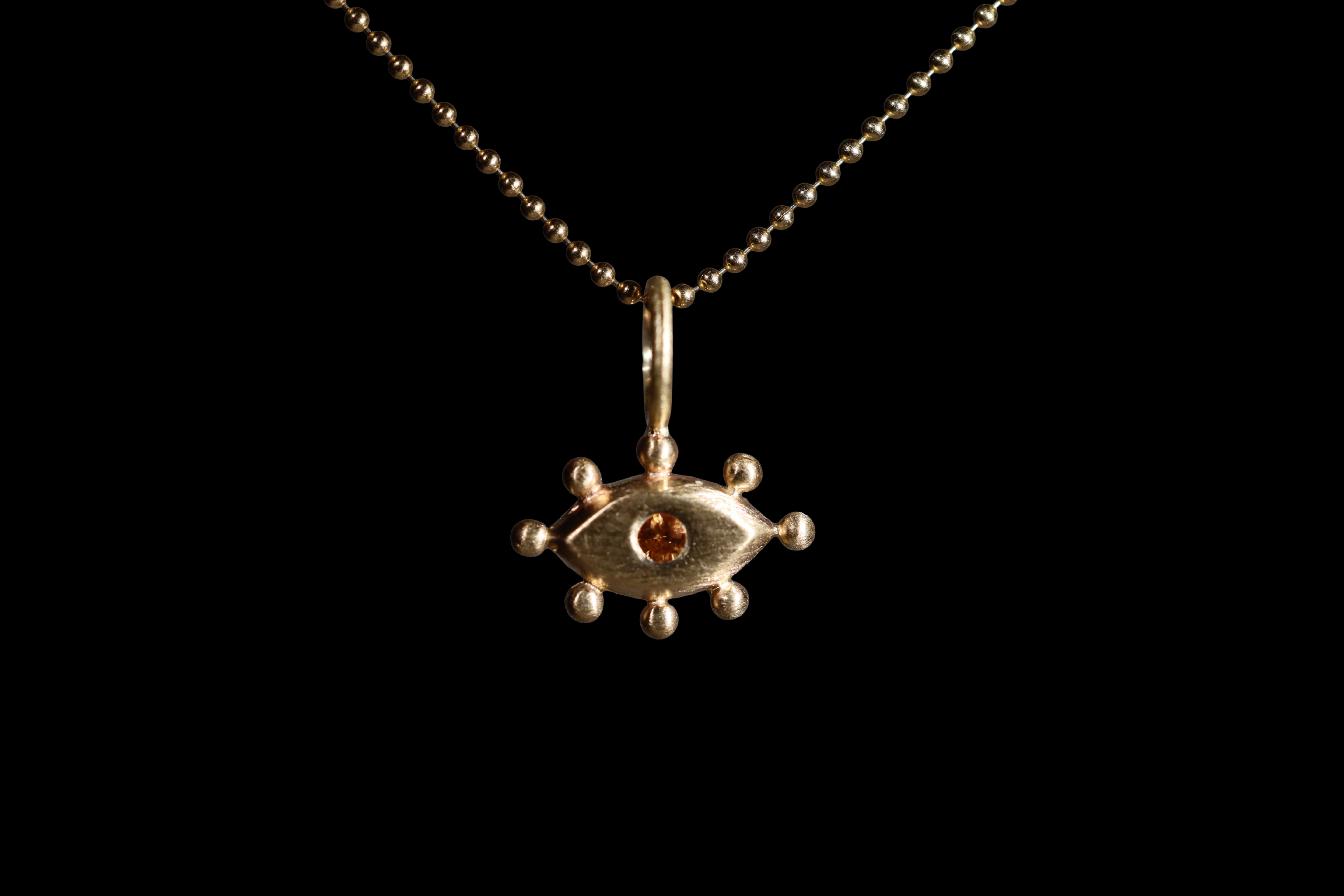 Gold pendant with with an eye design and orange gemstone on a black background