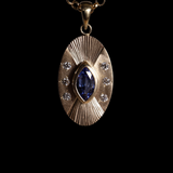 Front view of 14k yellow gold portal charm.  Tall oval shaped with central set blue marquise sapphire,  Three white diamonds on each side of the central stone  and engraved lines radiating up and down.