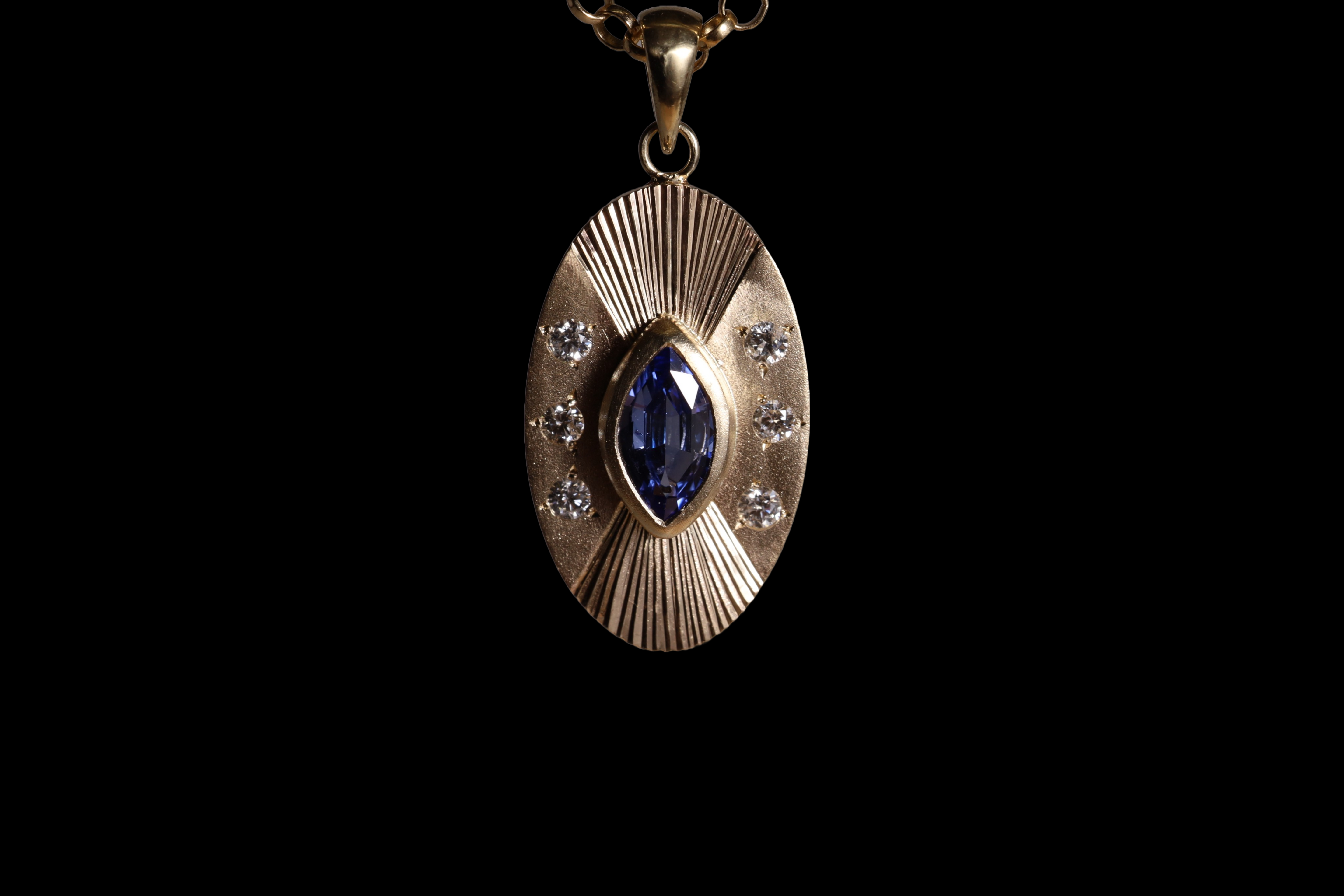 Front view of 14k yellow gold portal charm.  Tall oval shaped with central set blue marquise sapphire,  Three white diamonds on each side of the central stone  and engraved lines radiating up and down.