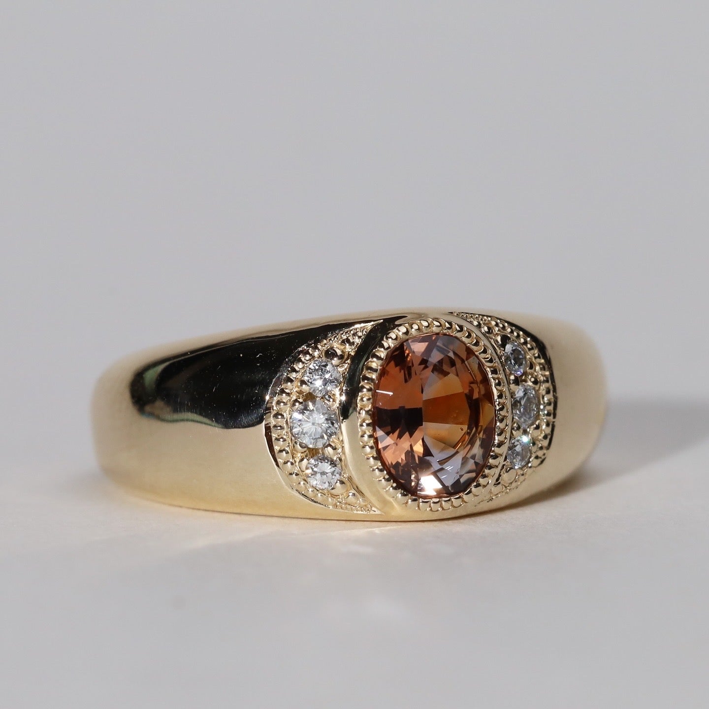 three quarter view of gold ring with central orange sapphire flanked by diamonds.