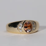 three quarter view of gold ring with central orange sapphire flanked by diamonds.
