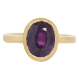 Front view of 18k yellow gold ring with central grape colored sapphire in tall solid setting.