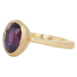 Another three quarter view of 18k yellow gold ring with central grape colored sapphire in tall solid setting.