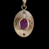 Front view of 14k yellow gold portal charm.  Circular shaped with central set pink sapphire, white diamonds set at the four compass points and engraved lines radiating from the central stone.