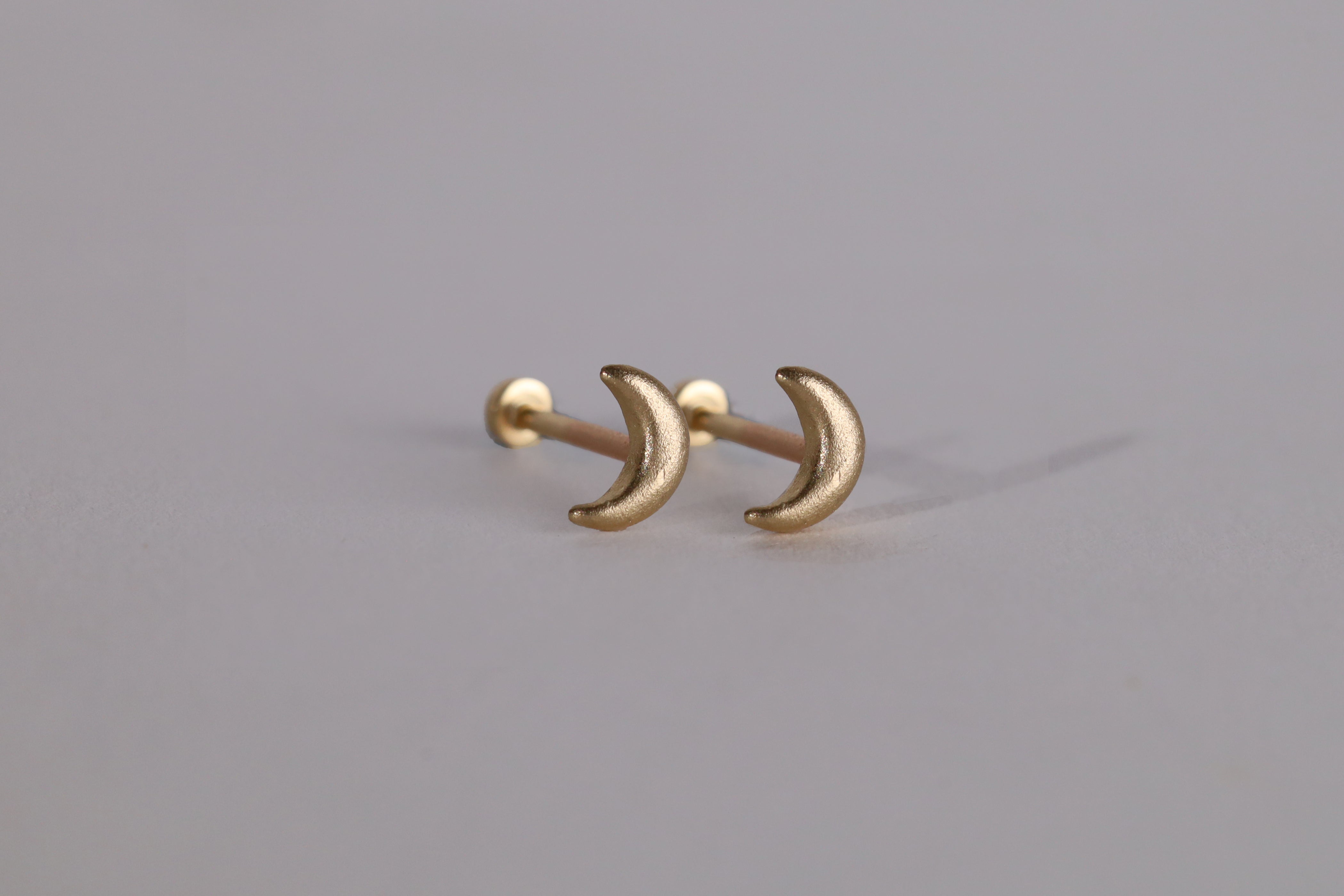 A pair of small 14k crescent moon shaped earrings on an off white background.