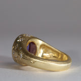 Gold signet style ring with large central purple sapphire, engraved with stars and comets, some set with diamonds. Rear view facing left.