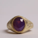 Gold signet style ring with large central purple sapphire, engraved with stars and comets, some set with diamonds.  Front view