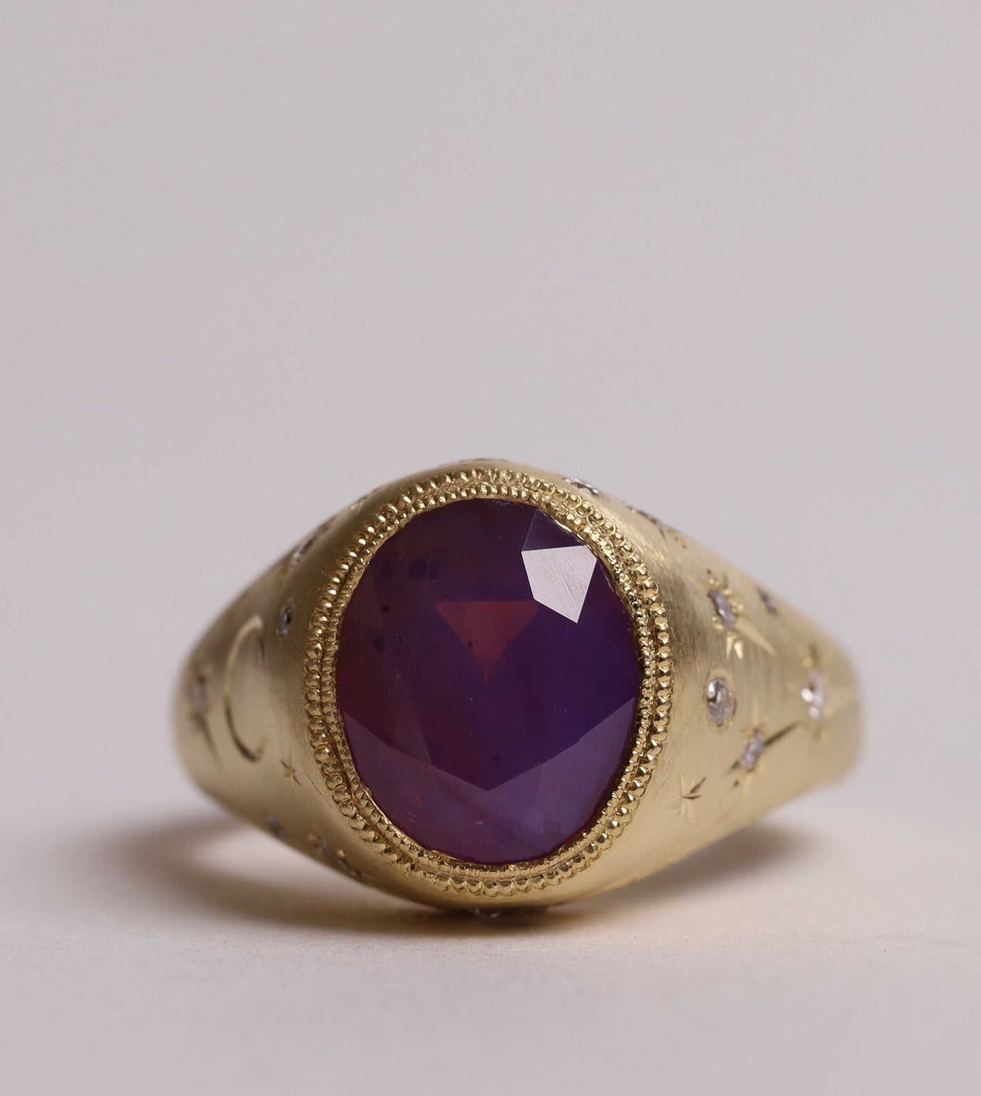 Gold signet style ring with large central purple sapphire, engraved with stars and comets, some set with diamonds.  Front view