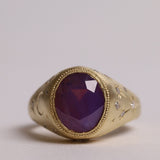 Gold signet style ring with large central purple sapphire, engraved with stars and comets, some set with diamonds.  Front view