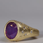 Gold signet style ring with large central purple sapphire, engraved with stars and comets, some set with diamonds. Side view facing left.